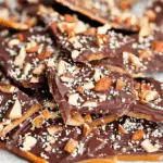 Close-up of Better Than Anything Toffee pieces topped with chopped almonds and sea salt on a parchment-lined tray.