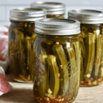 Jars of pickled okra in brine with garlic and spices, sealed with silver lids.