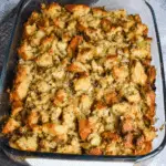 Grandma’s Thanksgiving Dressing baked golden brown in a glass casserole dish with chunks of bread, herbs, and vegetables.