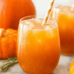 A chilled glass of magical Harry Potter pumpkin juice with ice and a striped straw, surrounded by fresh pumpkins.