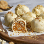 Close-up of No Bake Pumpkin Cheesecake Balls coated in white chocolate and topped with cookie crumbs on a wooden board.