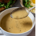 Perfect Turkey Gravy in a white bowl with a spoon lifting a portion, showing its smooth and creamy texture.
