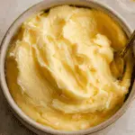 Creamy swirl of The BEST Honey Butter in a small ceramic bowl with a spoon.