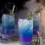 Vibrant Witches Brew Lemonade in tall glasses with crushed ice, garnished with rosemary and served with metal straws.