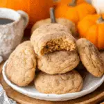 A plate of Pumpkin Pie Spice Cookies with one cookie bitten to reveal a soft, spiced center, surrounded by pumpkins and a cup of coffee.