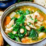 A rustic bowl of Tuscan Chicken Soup filled with shredded chicken, white beans, kale, carrots, and herbs in a savory broth.