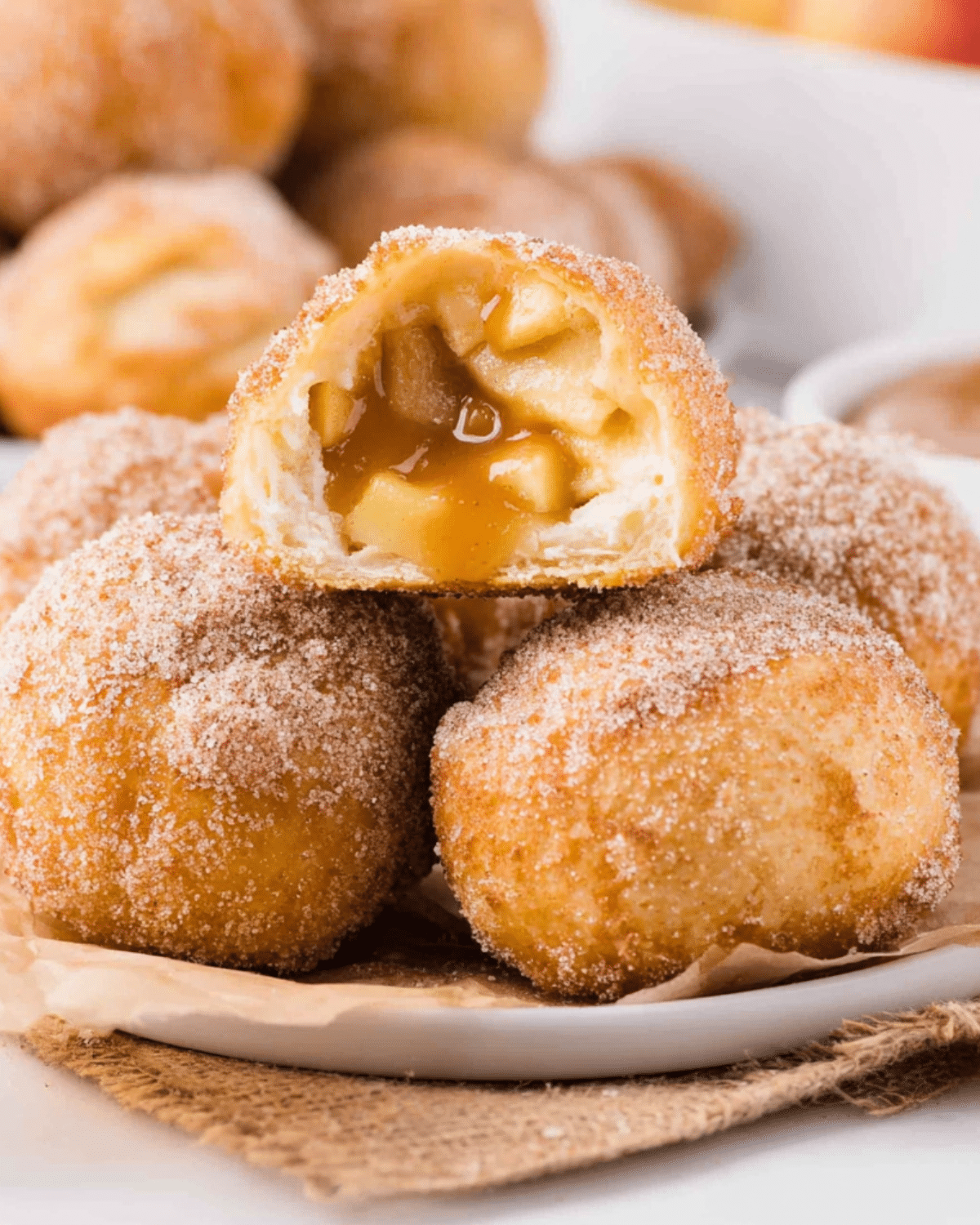 Caramel apple pie bombs coated in cinnamon sugar, with one cut open to reveal a gooey caramel and apple filling.