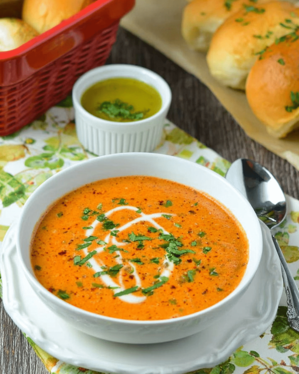 Easy creamy tomato soup in a white bowl, garnished with a swirl of cream and chopped herbs, served with fresh bread and olive oil on the side.