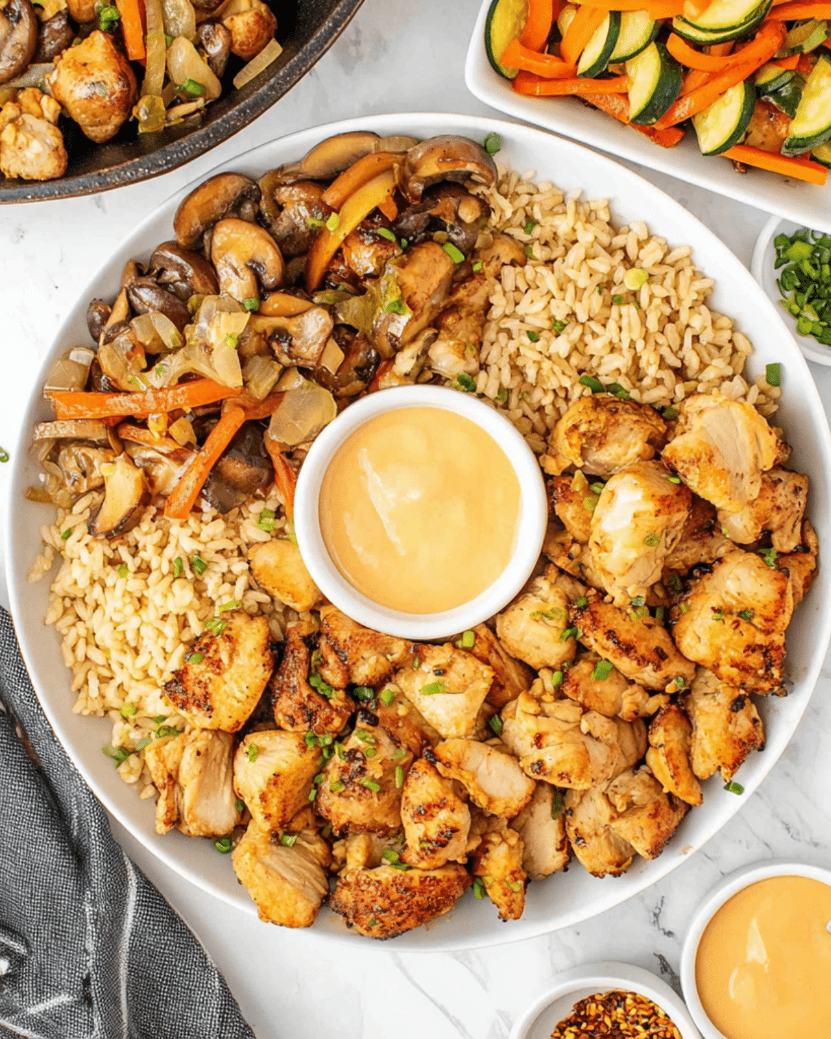Plate of Benihana hibachi chicken served with fried rice, sautéed mushrooms and vegetables, and a creamy dipping sauce.