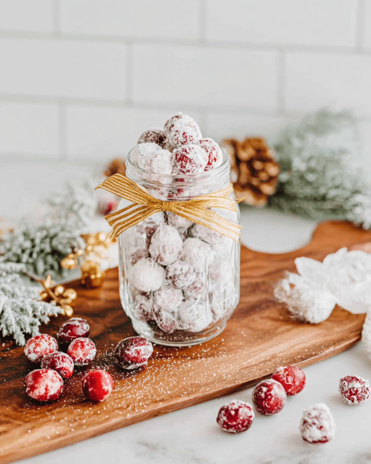 Glass jar filled with candied cranberries coated in sugar, surrounded by festive holiday decor.