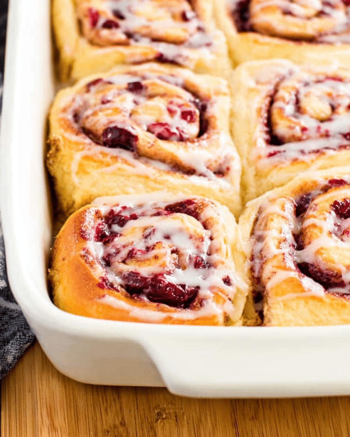 Cranberry orange sweet rolls in a white baking dish, topped with a light glaze.