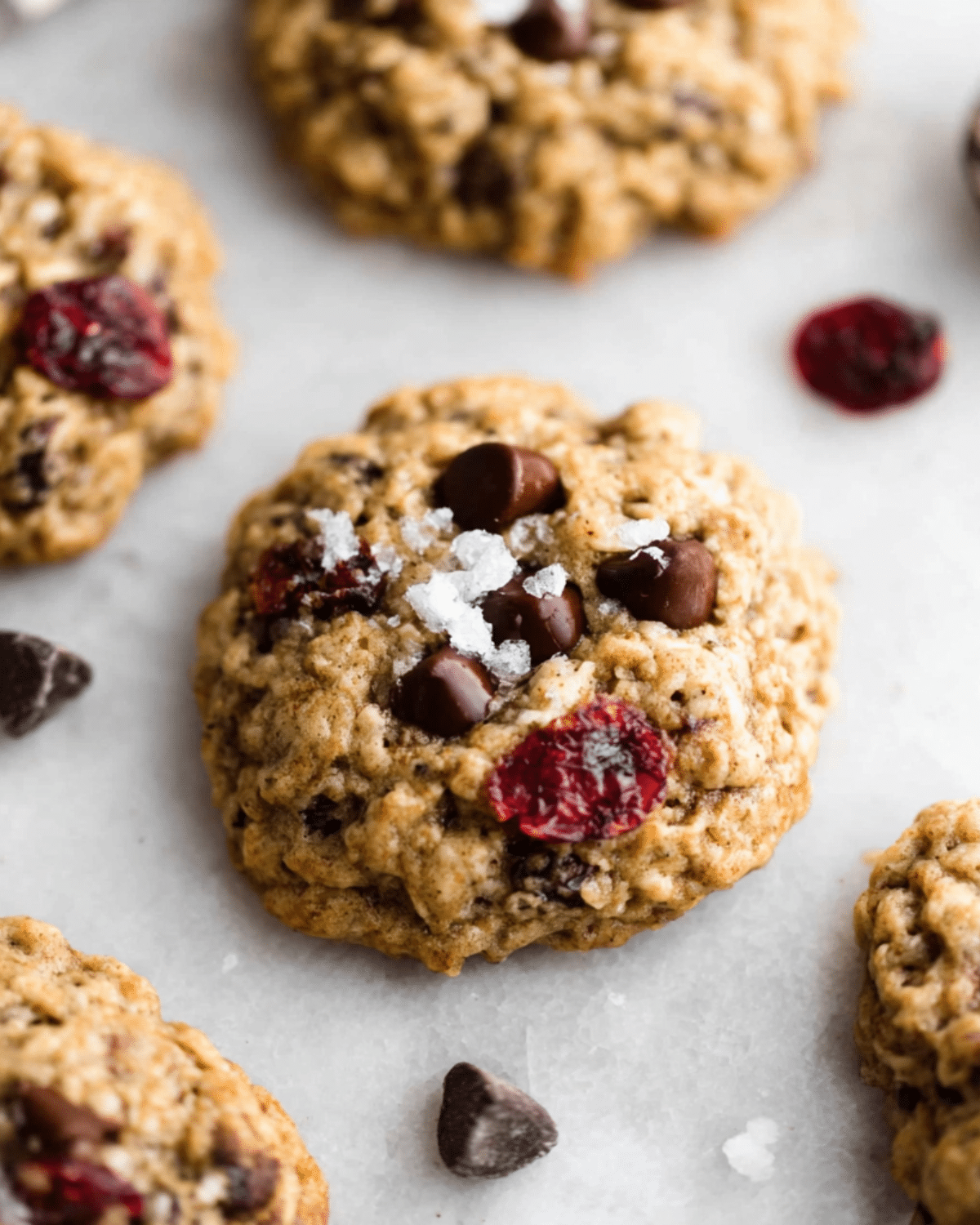 Dark chocolate cranberry oatmeal cookies with sea salt flakes on a light surface.