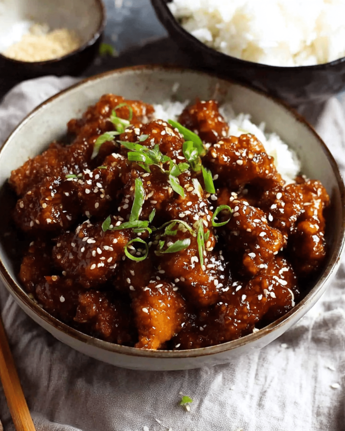 Bowl of General Tso chicken served over white rice, garnished with sesame seeds and sliced green onions.