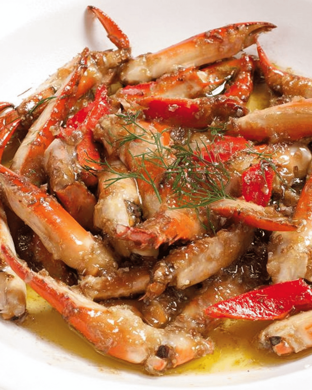 Marinated Louisiana crab claws coated in a buttery garlic sauce, garnished with herbs on a white plate.