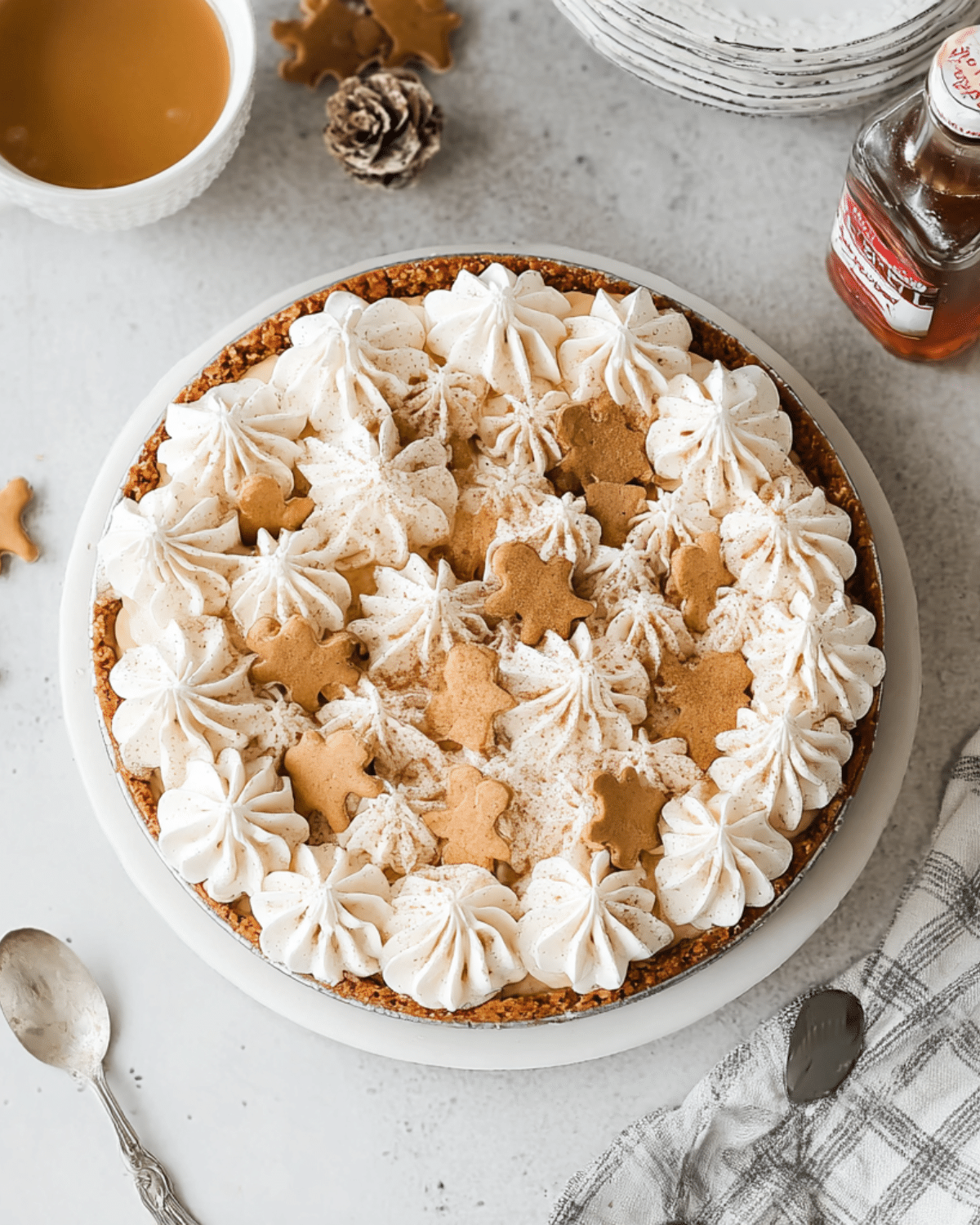 No bake gingerbread cheesecake topped with whipped cream and mini gingerbread cookies on a white plate.