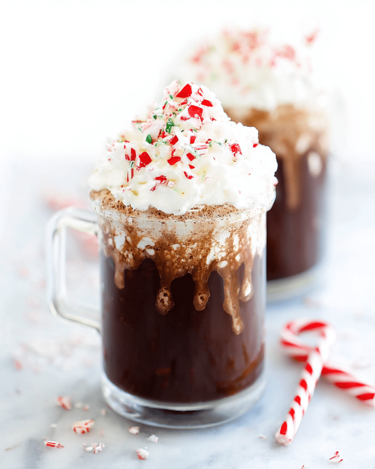 Glass mug of peppermint hot chocolate topped with whipped cream and crushed candy canes.