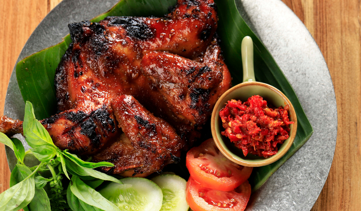 Harissa Honey Chicken: Grilled chicken on a plate, glazed with spicy-sweet harissa honey, accompanied by tomatoes and assorted vegetables, showcasing a delightful mix of North African spices and natural sweetness.