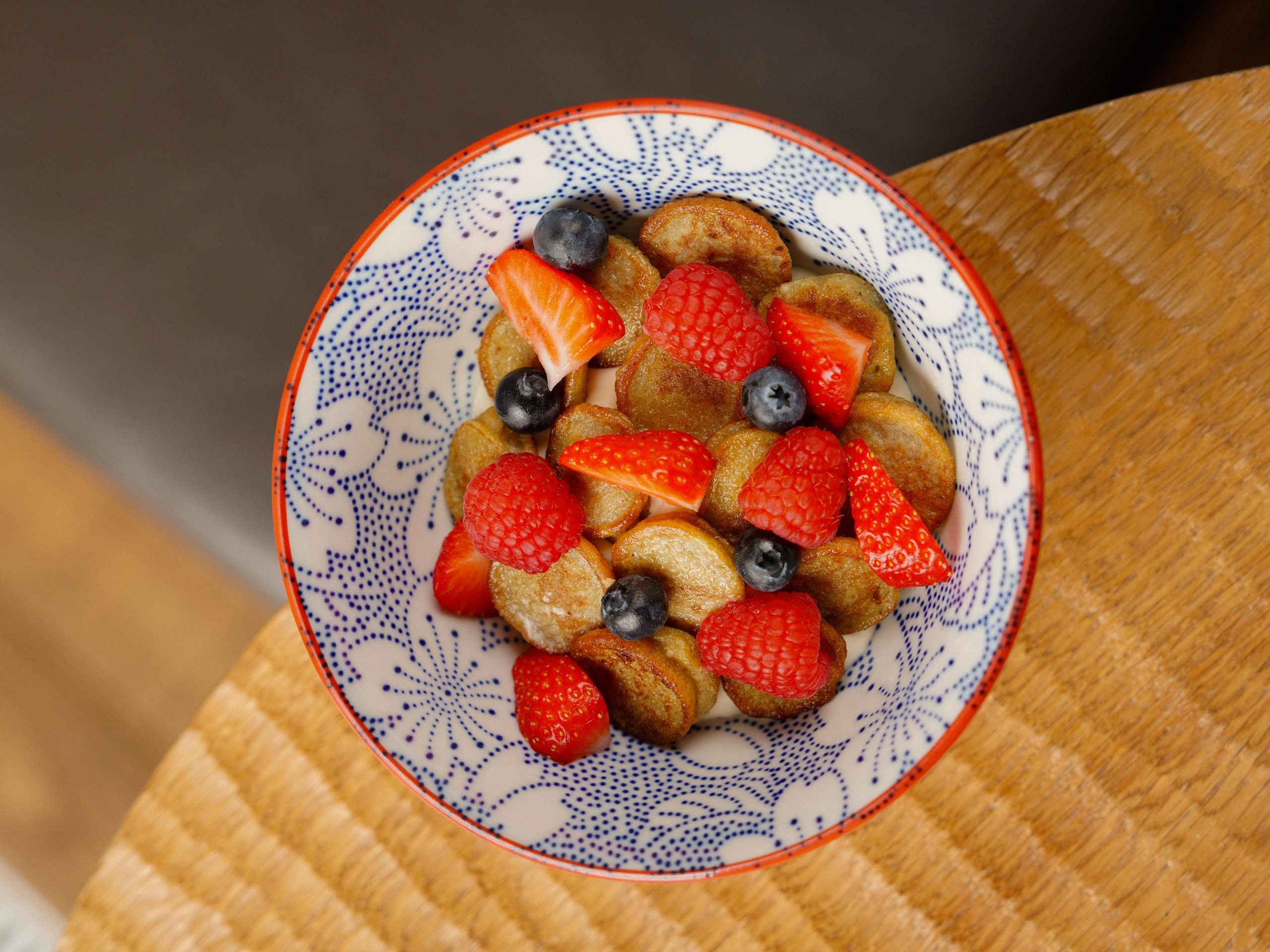 A plate of mini pancakes topped with fresh strawberries and blueberries, served on a white plate.