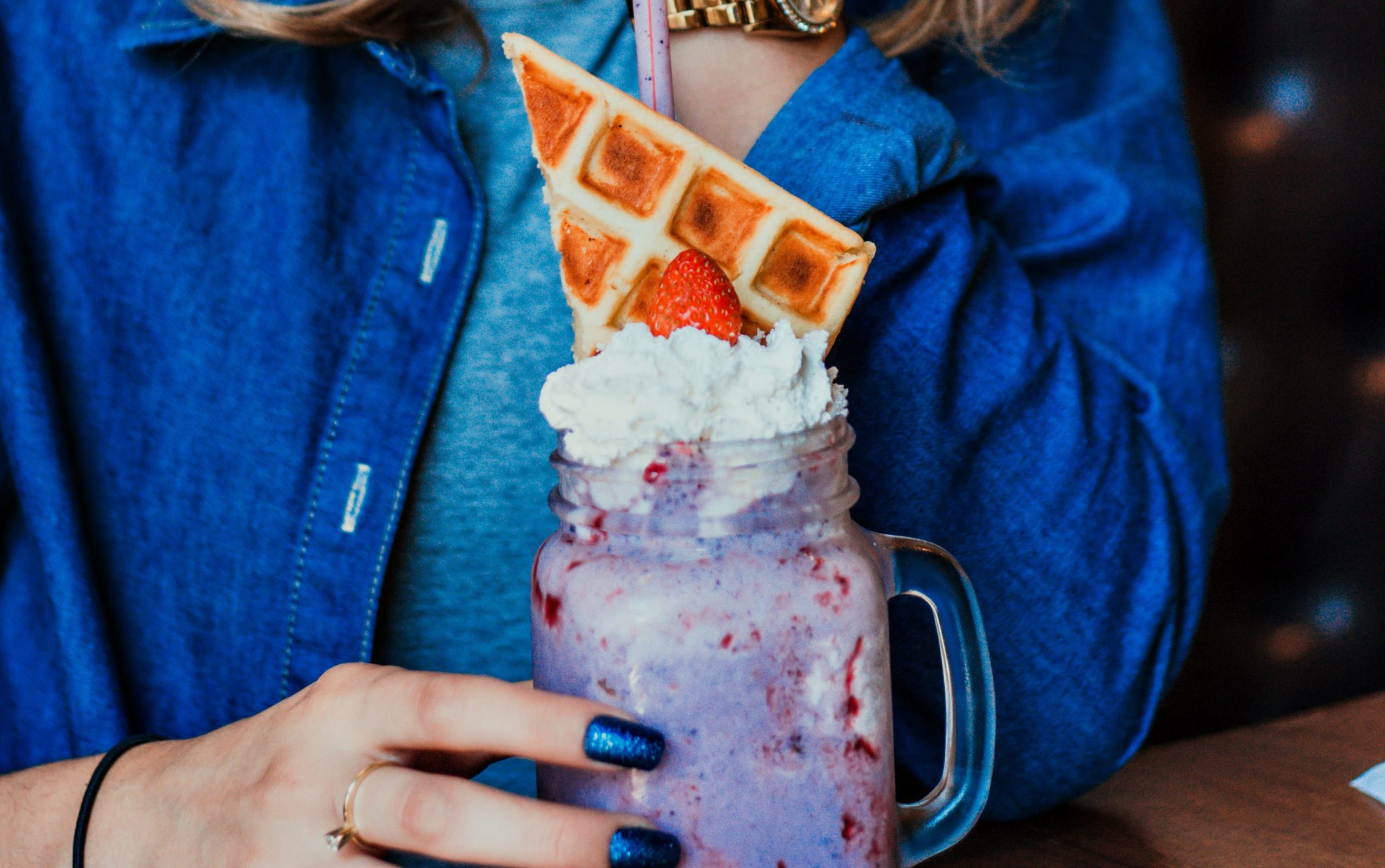 A woman is pictured holding a delightful waffle accompanied by a GRIMACE SHAKE , perfectly embodying the essence of a Homemade Grimace Shake. This image captures the art of Creamy Shake Preparation, showcasing a Delicious Milkshake Recipe that anyone can recreate at home. The milkshake, with its velvety texture, is a testament to the Velvety Shake Mix technique, making it not just a treat for the taste buds but also a feast for the eyes. This scene is a perfect representation of the joy and simplicity of making your own Grimace Shake, blending both traditional and innovative flavors.