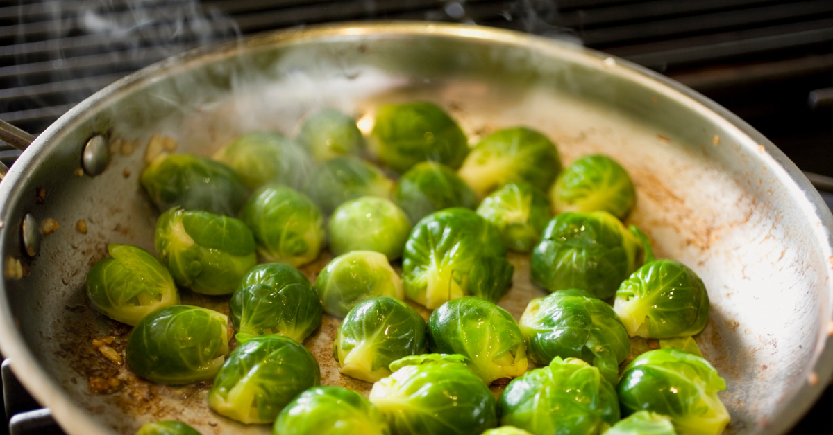 Brussels sprouts sizzling in a skillet on the stove, emitting steam as they cook.