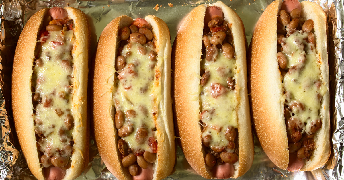 Four Oven-Cooked Hot Dogs topped with melted cheese and savory beans, beautifully arranged on foil, perfectly prepared and ready to be savored.