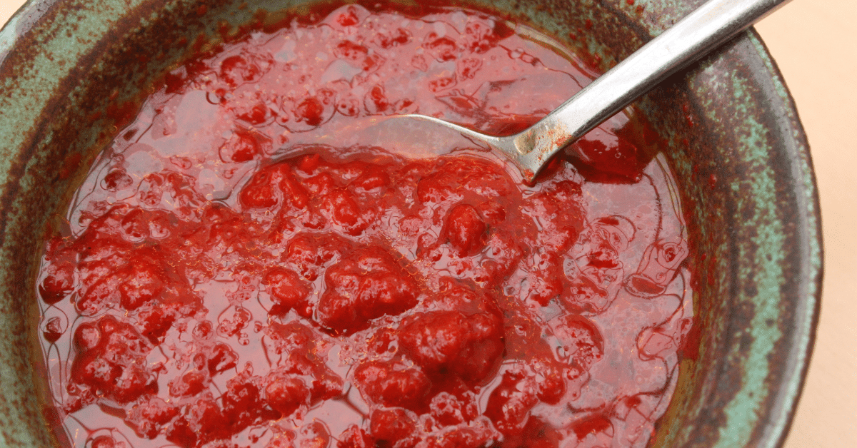 A bowl of red sauce with a spoon in it, topped with harissa.
