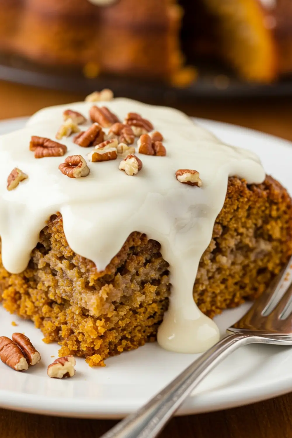 Moist slice of pumpkin oatmeal dump cake topped with glaze and chopped pecans on a white plate.