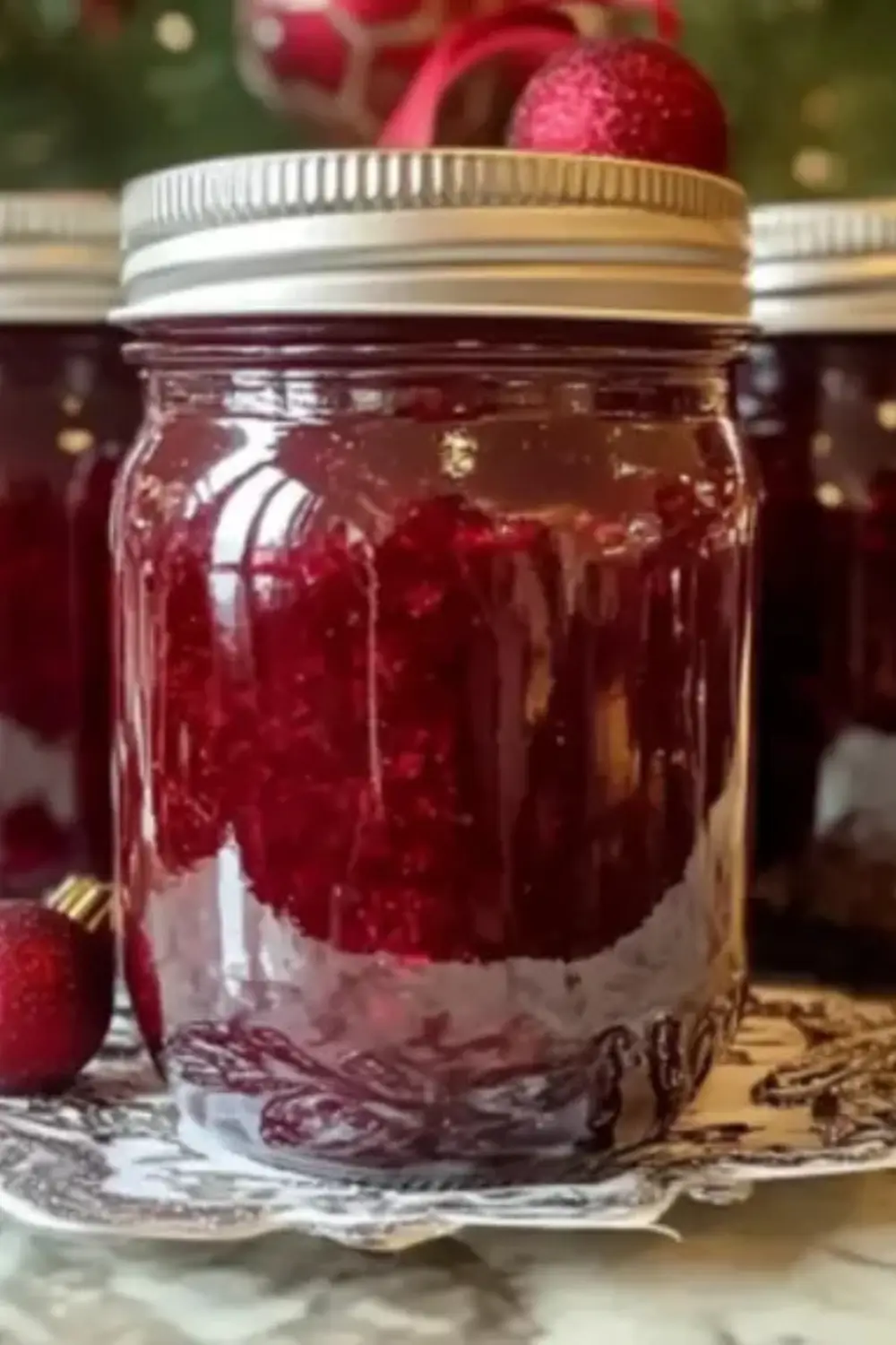 Jar of bright red homemade Christmas jam with festive decor in the background.