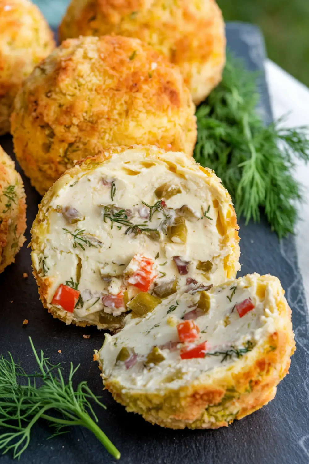 Creamy dill pickle cheese ball cut in half, filled with herbs, diced pickles, and peppers.