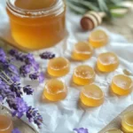 A collection of golden tea bombs infused with honey, neatly arranged on parchment paper with sprigs of fresh lavender nearby, and a jar of honey in the background. These Flu/Cold Tea Bombs are designed to dissolve in hot water, creating a soothing tea to help relieve flu and cold symptoms