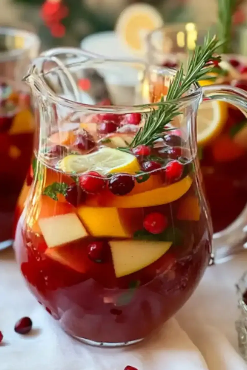 Festive holiday fruit punch with cranberries, citrus slices, and rosemary in a glass pitcher.