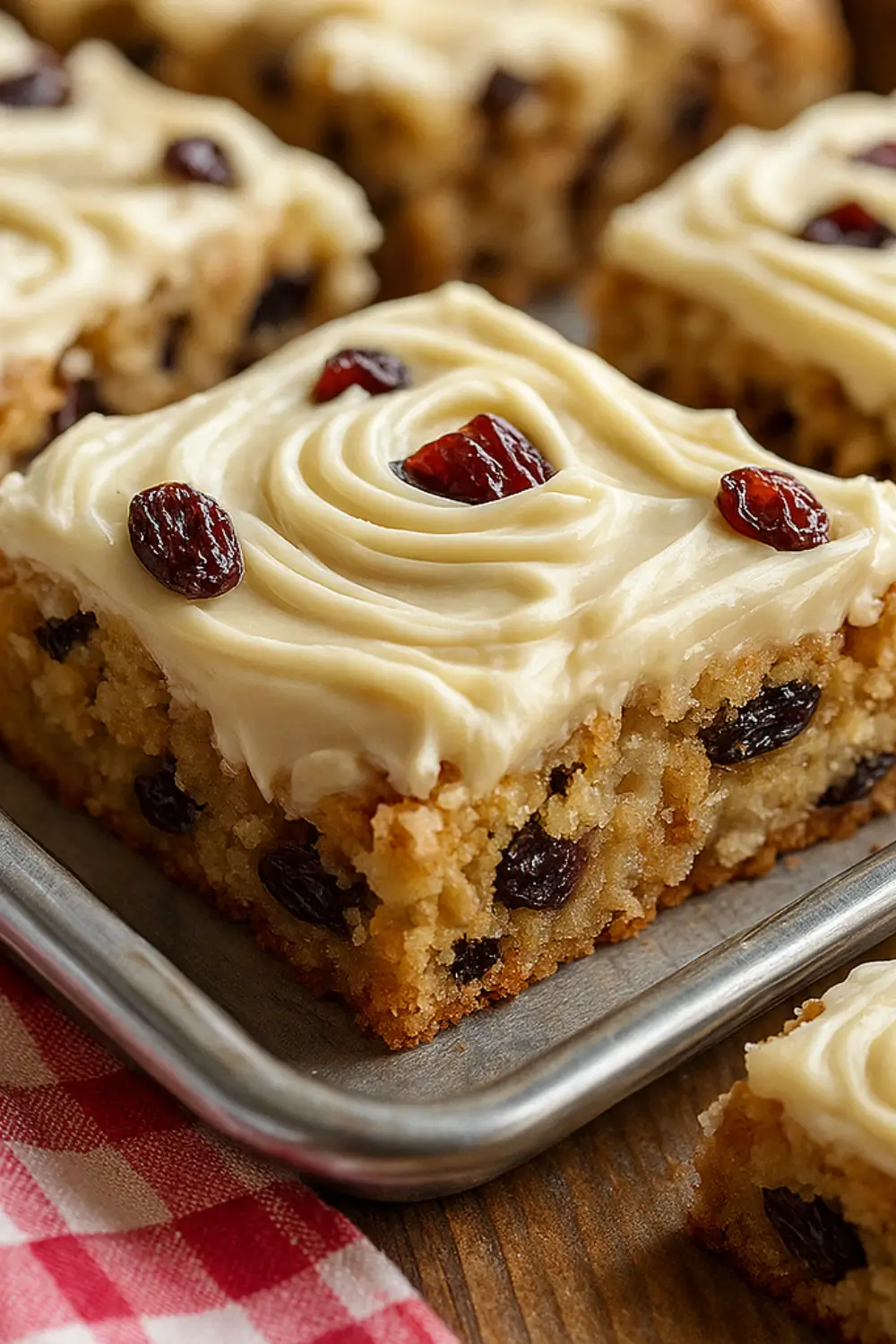 Moist oatmeal raisin cookie bars topped with swirled cream cheese frosting and garnished with raisins on a baking sheet.