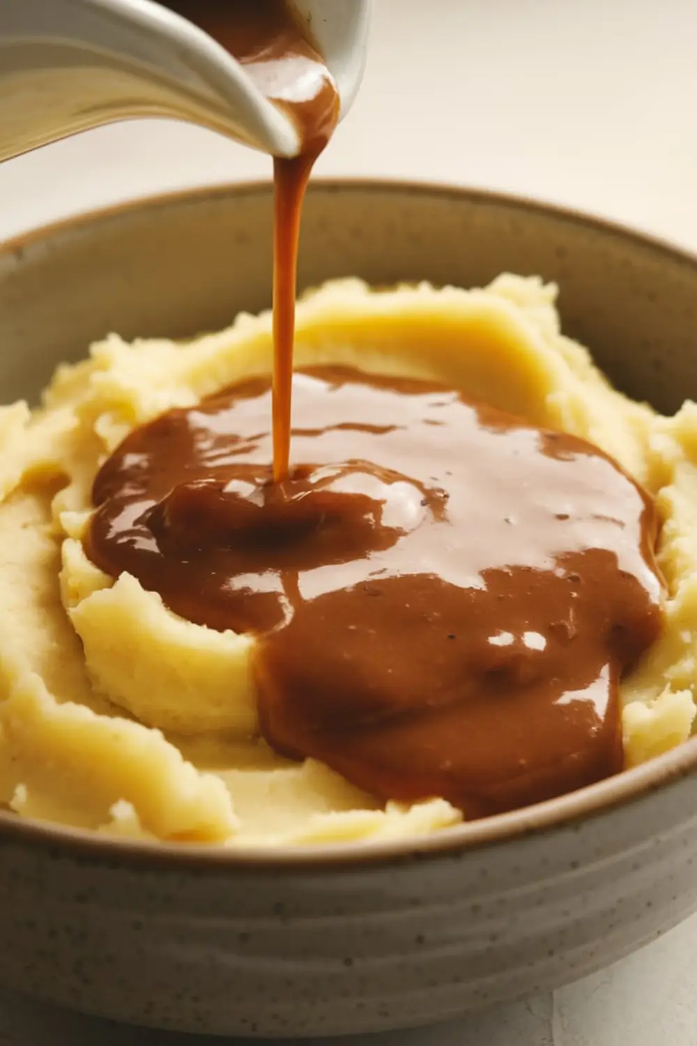 Rich brown KFC-style gravy being poured over creamy mashed potatoes in a ceramic bowl.