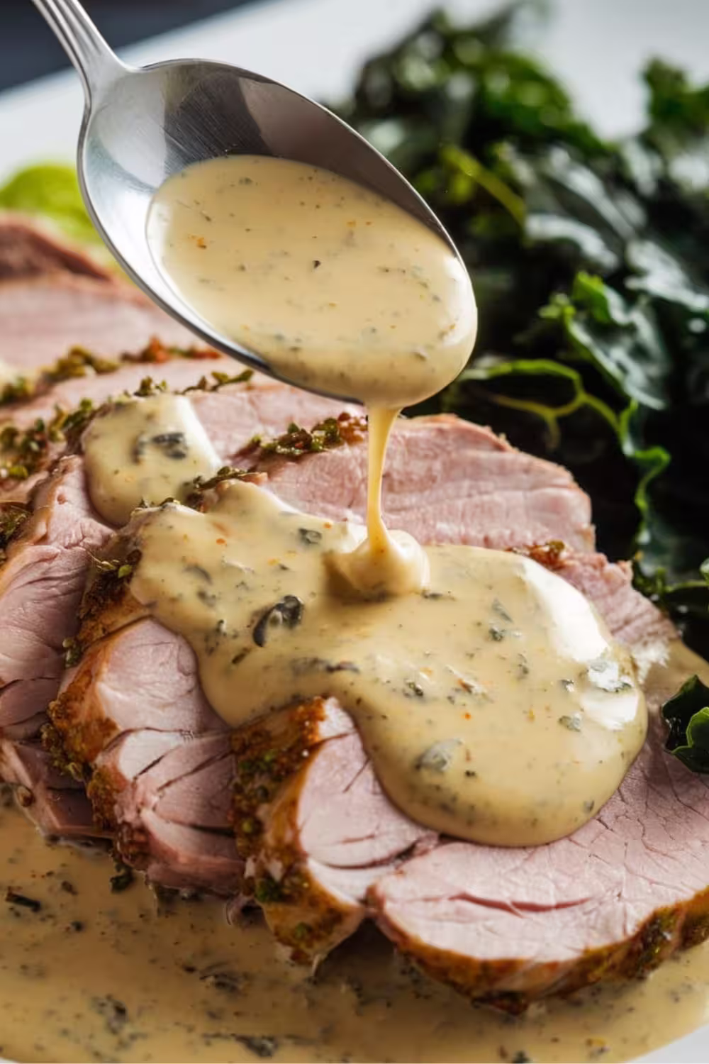 Sliced pork tenderloin topped with a creamy Dijon mustard sauce being drizzled from a spoon.