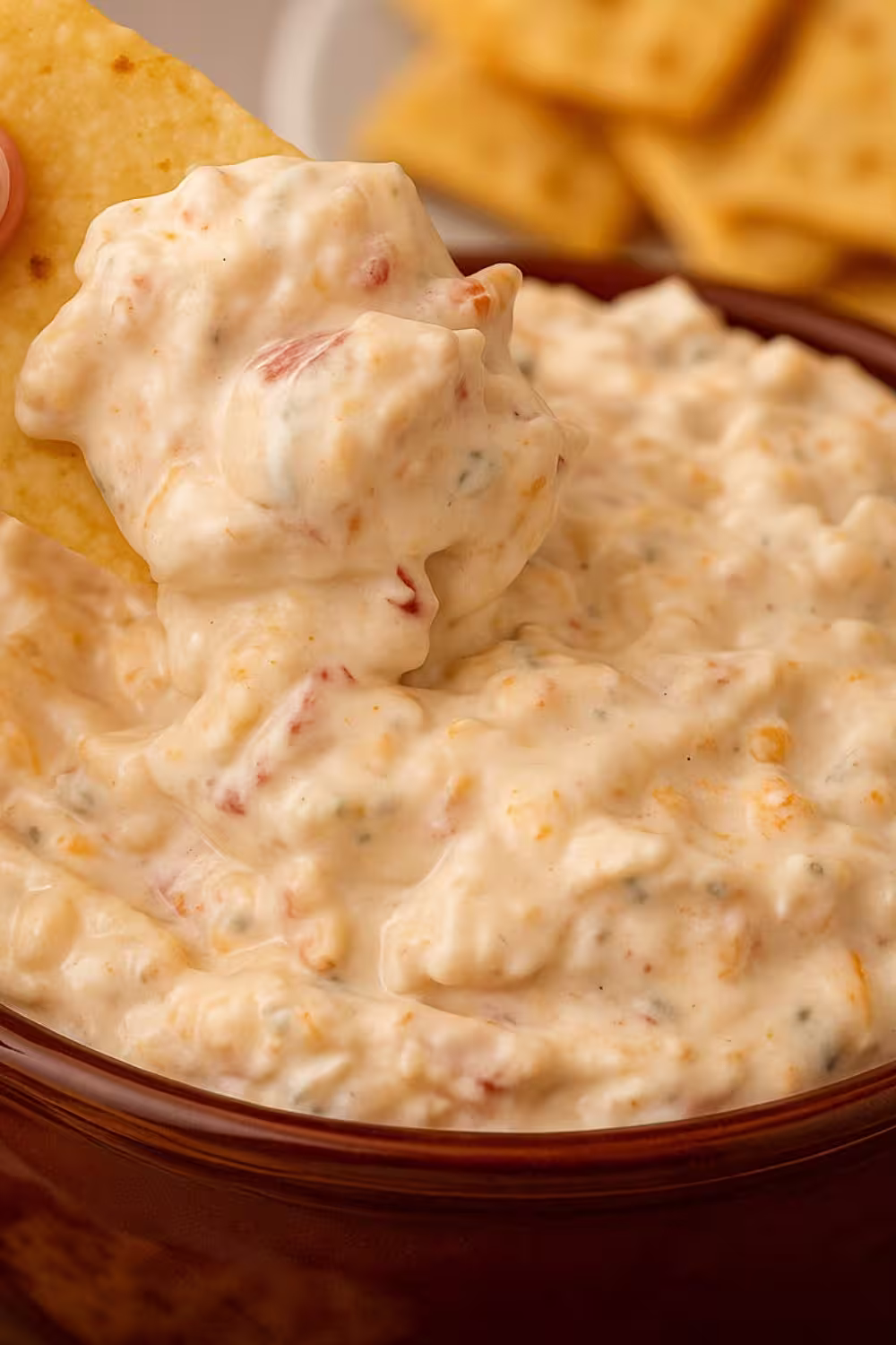 Creamy cheese dip with tomatoes and shredded cheese served in a brown bowl, surrounded by tortilla chips.