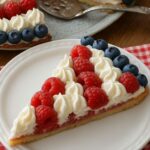 American Flag Fruit Pizza decorated with fresh raspberries, blueberries, and whipped cream in a patriotic pattern.