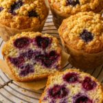 Gluten-free blueberry muffins with crumb topping, one sliced open to reveal a moist interior filled with juicy blueberries.