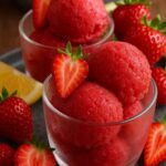 Refreshing strawberry sorbet served in a glass bowl, garnished with fresh strawberries and a lemon wedge.