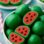 Vibrant green watermelon truffles with a red center and chocolate chip "seeds," arranged in a white bowl.