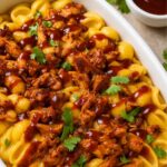 Creamy mac and cheese topped with tender BBQ chicken, garnished with fresh cilantro in a white casserole dish.