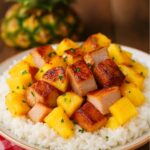 Tender chunks of pineapple and pork loin served over fluffy white rice, garnished with fresh parsley, with a whole pineapple in the background.