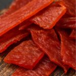 Slices of homemade ground venison jerky on a rustic wooden board.