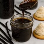 Homemade vanilla bean paste in a glass jar with vanilla pods and piped cookies in the background.