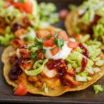 Crispy BBQ chicken tostadas topped with shredded lettuce, sour cream, and diced tomatoes.