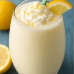Glass of frozen creamy lemonade topped with whipped cream, lemon zest, and a lemon slice.