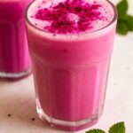 Bright pink Starbucks Dragon Drink in a clear glass, topped with dragon fruit powder and served with fresh mint leaves.