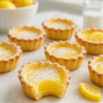 Baby lemon impossible pies topped with powdered sugar and a bite revealing creamy lemon filling