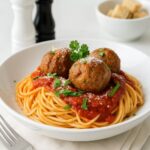 Spaghetti topped with Cheesecake Factory meatballs and marinara sauce on a white plate