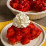 Slice of homemade strawberry pie topped with whipped cream on a white plate