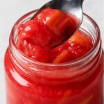 Spoonful of chunky rhubarb compote being lifted from a jar